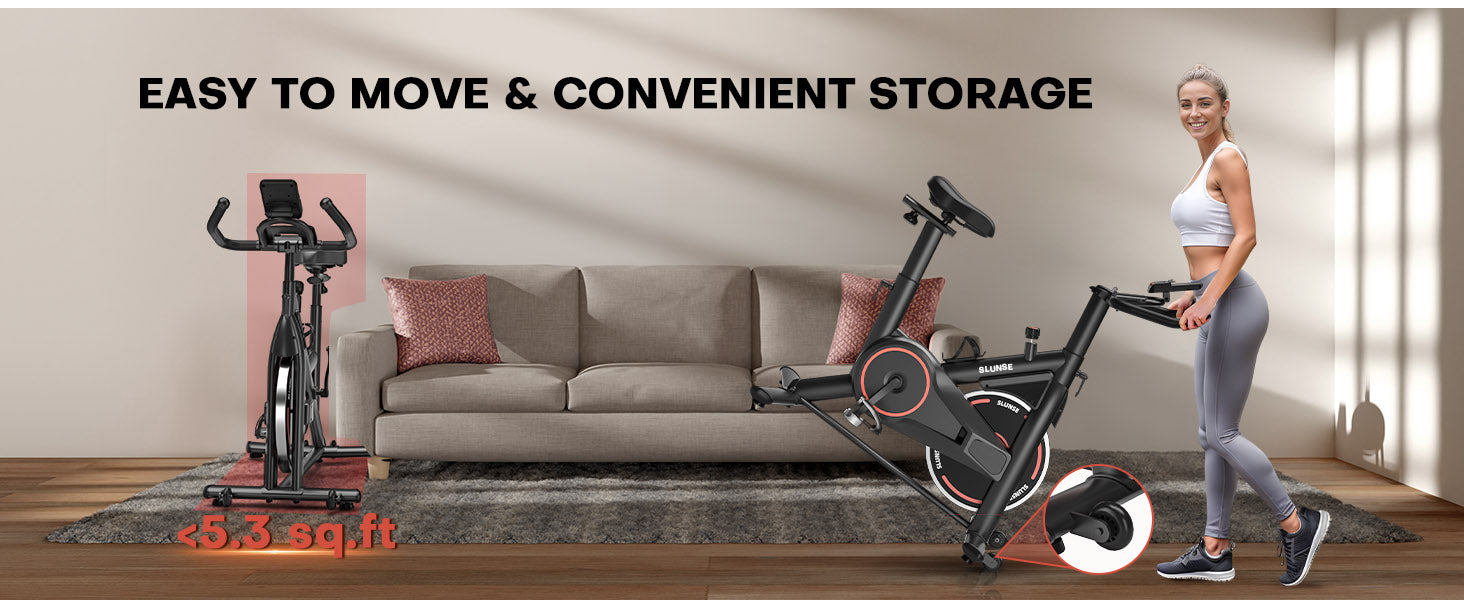 En motionscykel med en kvinde stående ved siden af, placeret på et trægulv i en stue.